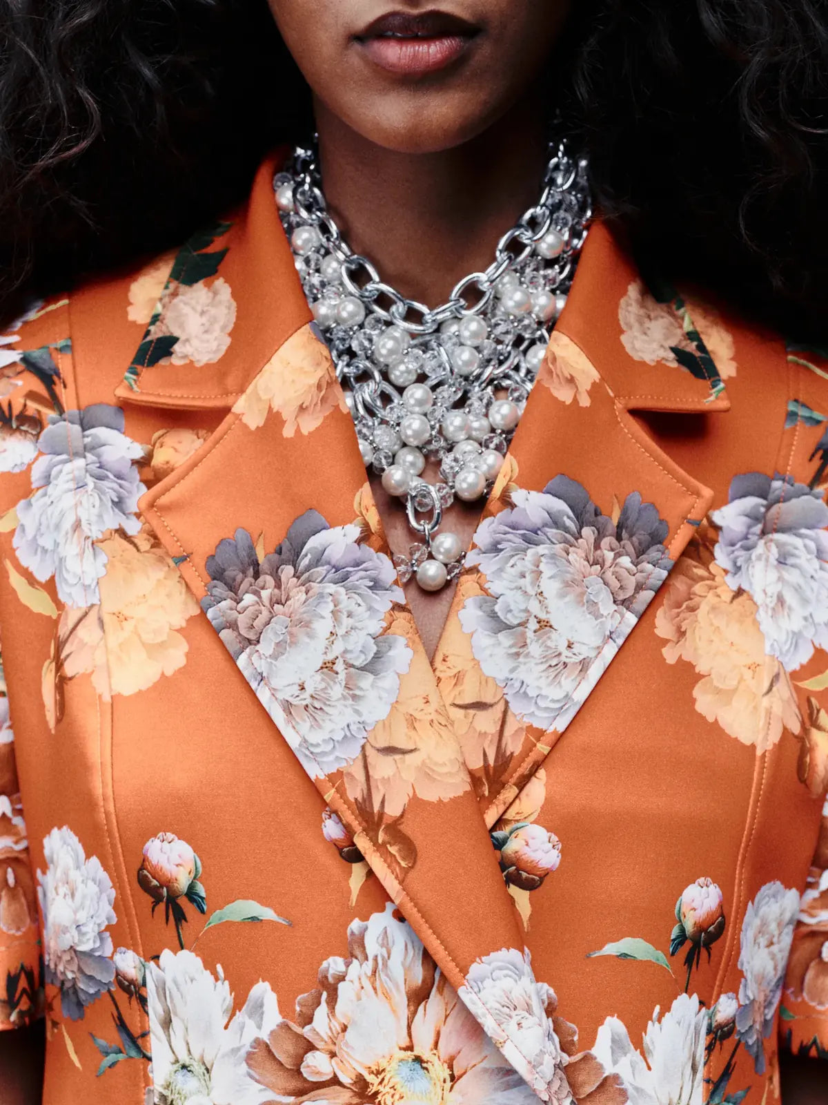 Kampagne Dancing Flowers: Detail eines Damen-Blazers mit Blütenprint, dazu eine mehrreihige Perlenkette.