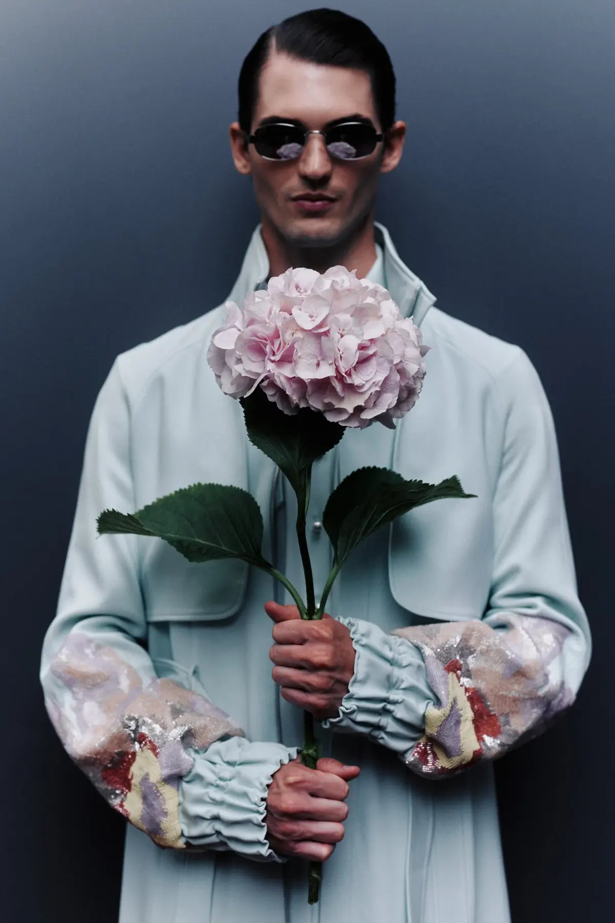 Kampagne Dancing Flowers: Herren-Mantel in Mint mit besticktem Ärmelbesatz, dazu eine Hortensienblüte in den Händen.