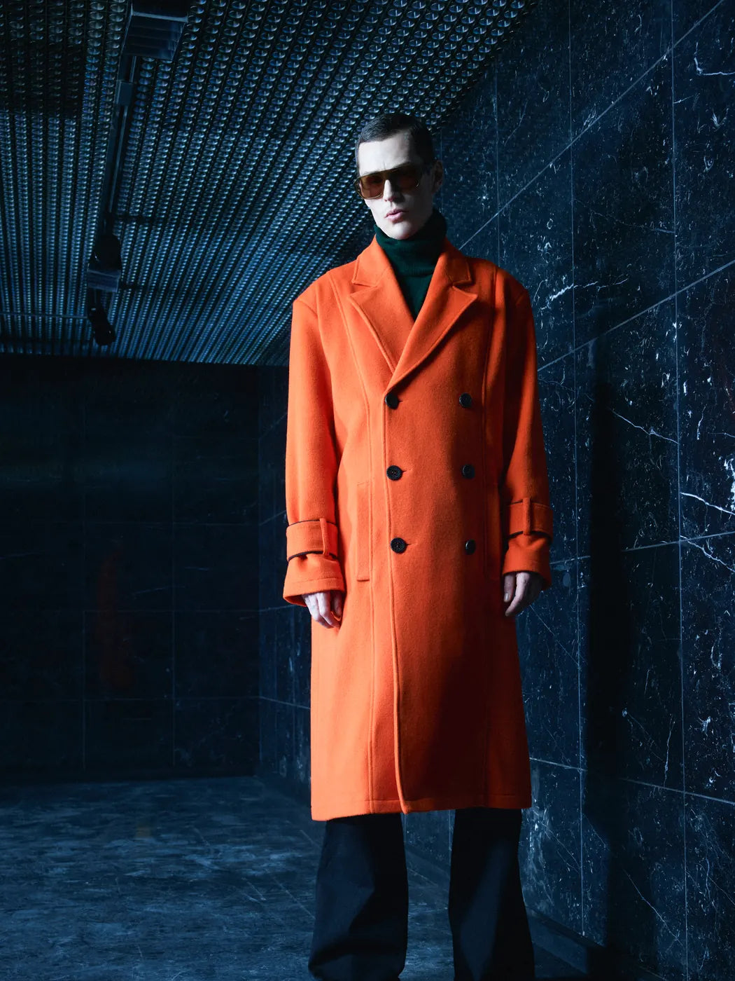 Model trägt Herren-Mantel aus Wolle und Alpaka in Orange, zweireihig mit Reverskragen und Kontrastknöpfen in Schwarz, Vorderansicht.
